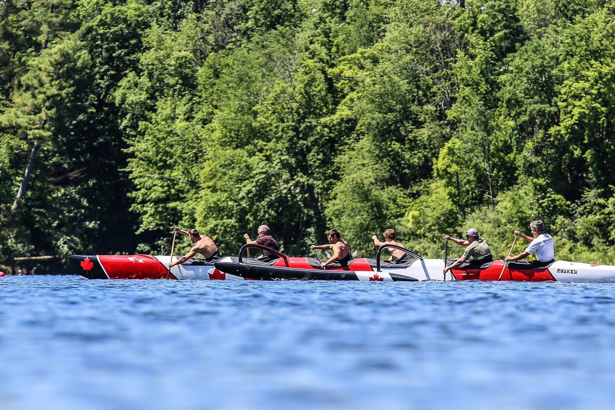 Two Outrigger Zone OC6 canoes in Canadian maple-leaf livery paddling on a calm forest-lined lake